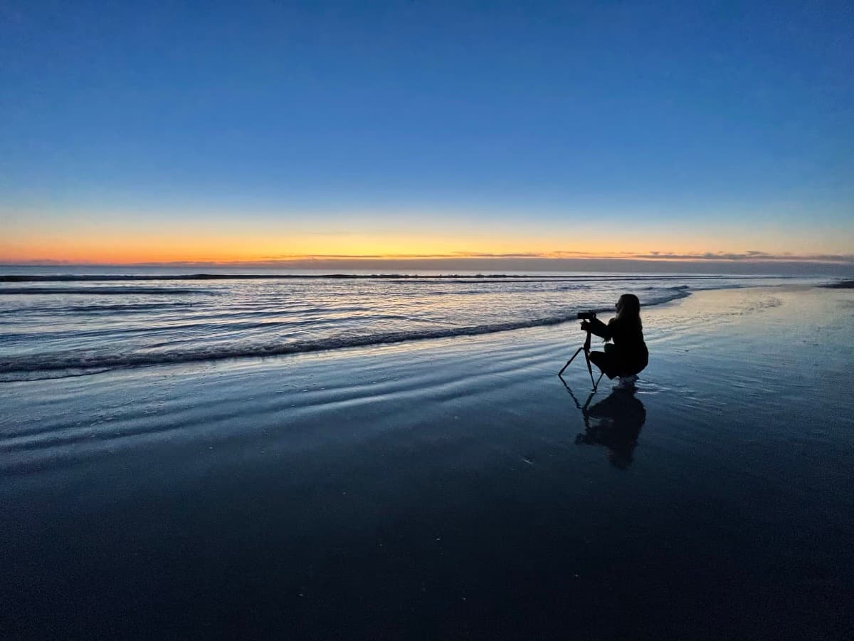 Una fotógrafa con trípode en la orilla del mar al atardecer