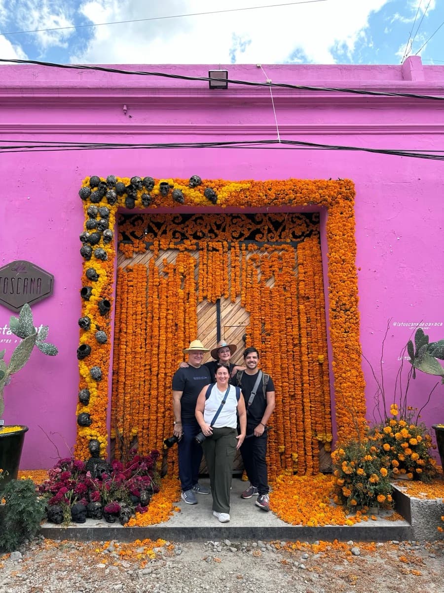 Tres personas frente a un arco de flores de cempasúchil en una pared rosa
