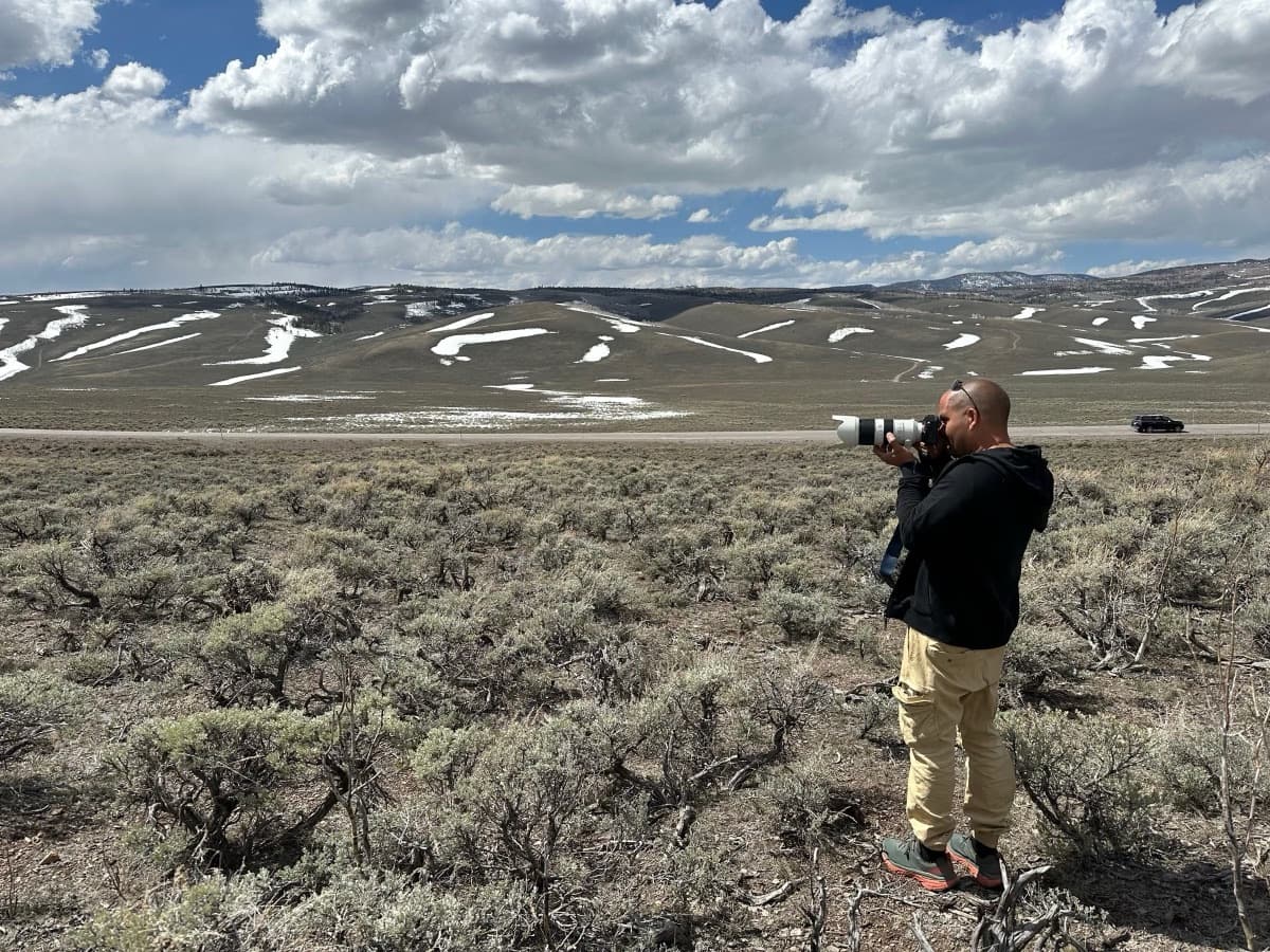 Un fotógrafo con teleobjetivo en una pradera de artemisa con montañas al fondo
