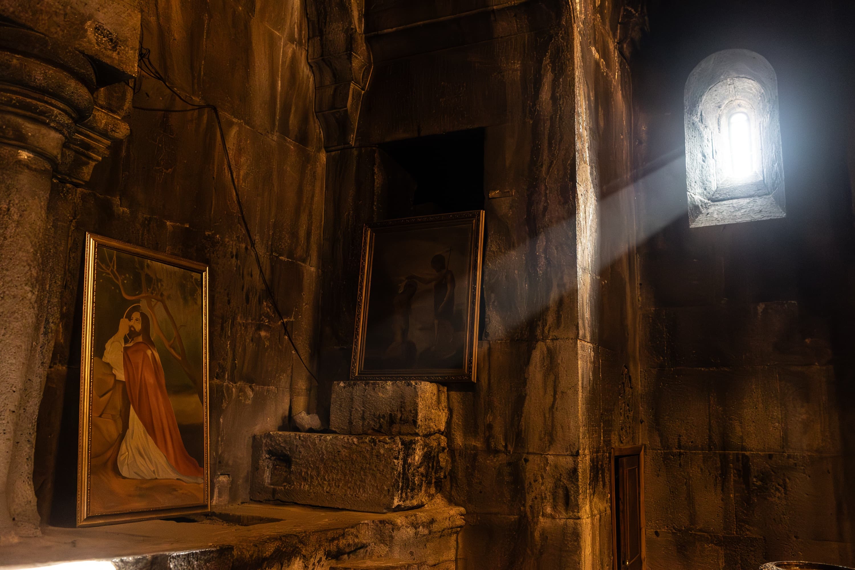 Un rayo de luz entra por el ventanuco de un monasterio de piedra, Armenia