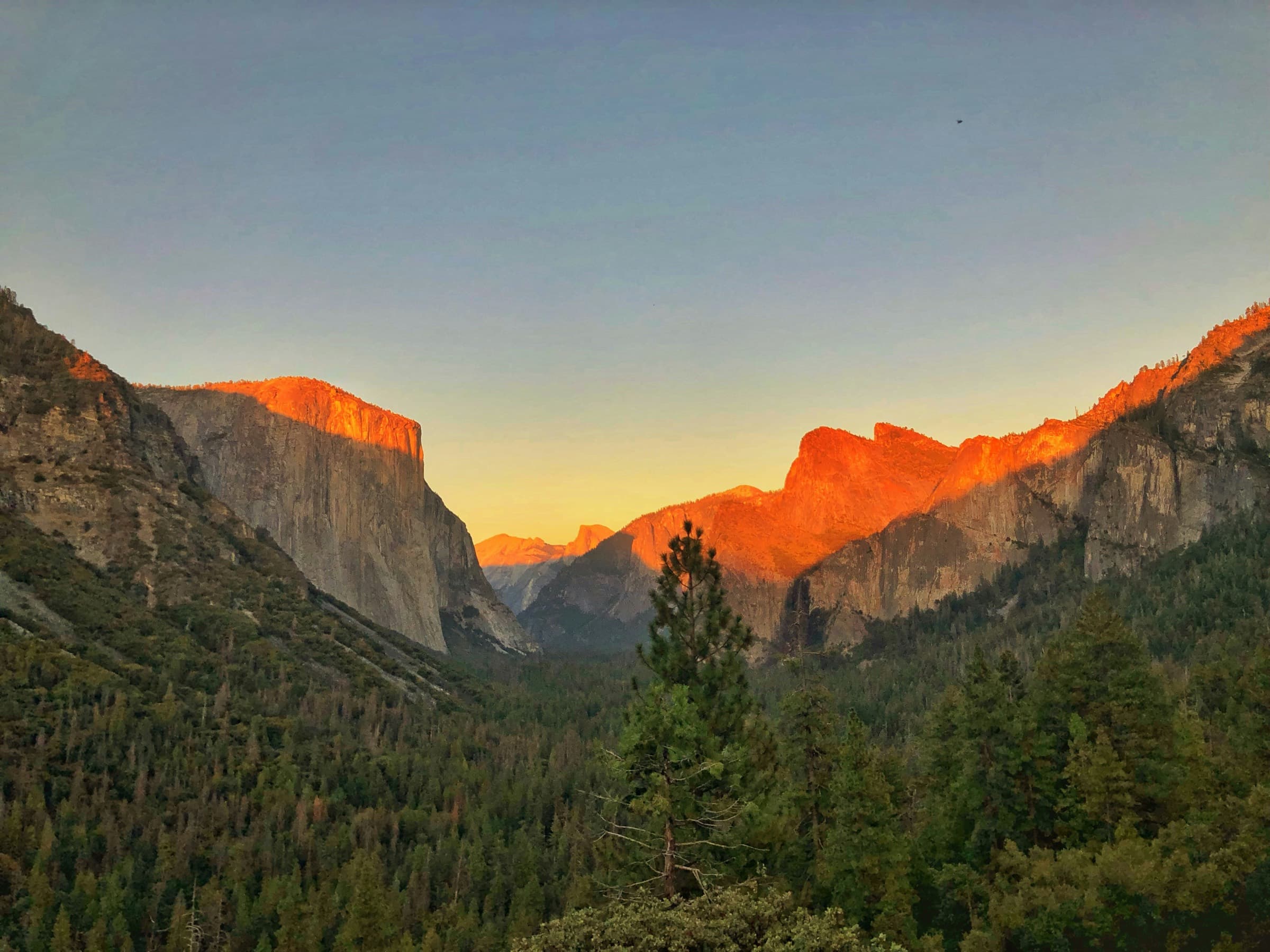 El valle de Yosemite desde Tunnel View al amanecer, con la primera luz naranja en la cima de El Capitán y Half Dome recortado al fondo.