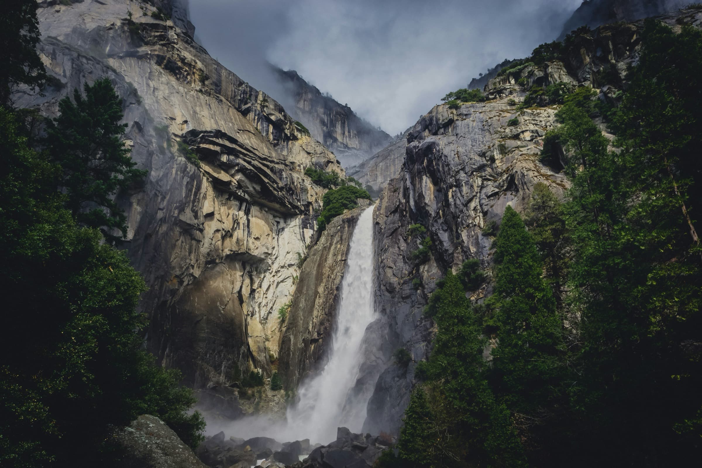 Una cascada cayendo entre paredes de granito, con niebla en lo alto del cañón.
