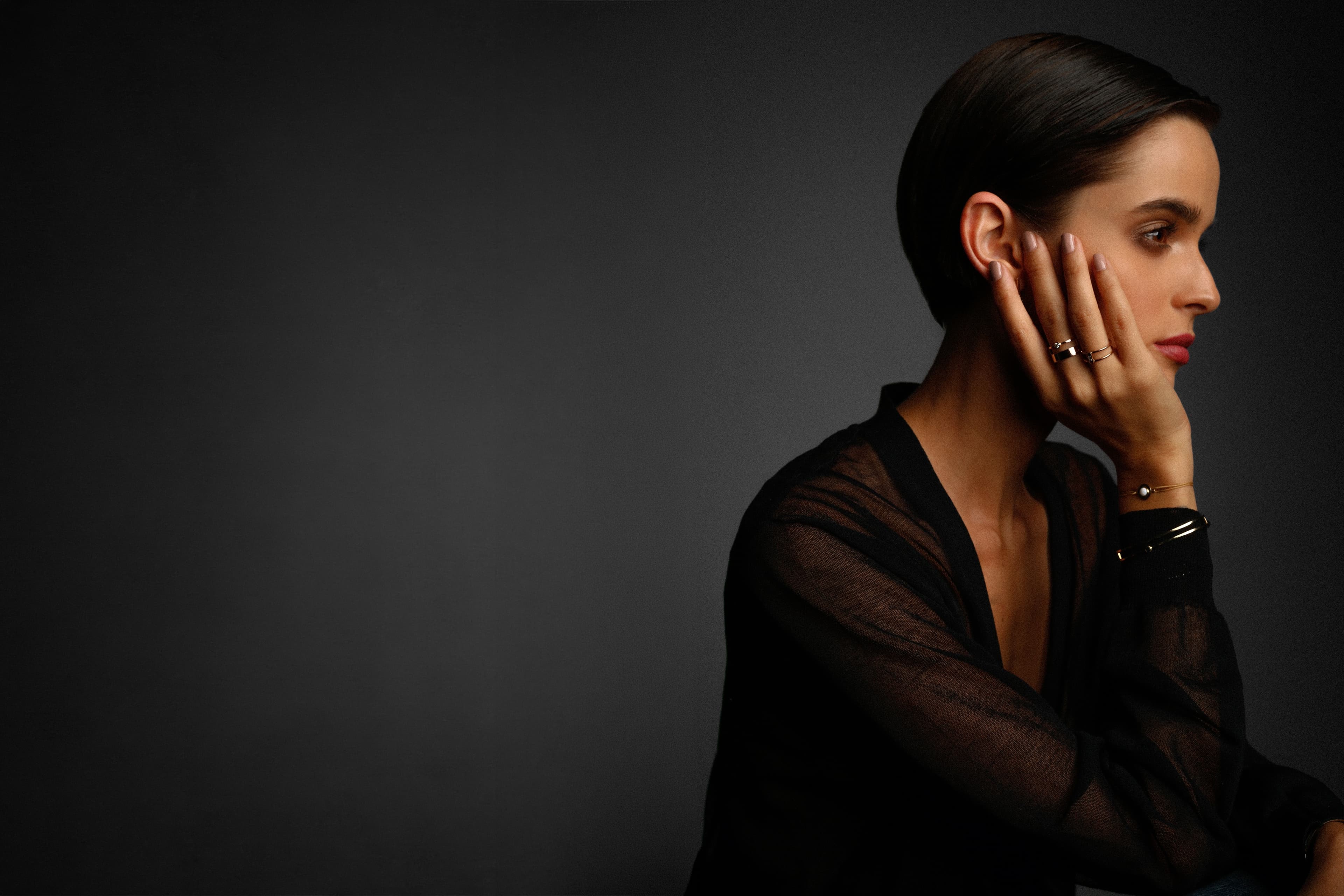 Retrato en clave baja: una mujer de perfil, con la mano en la mejilla, sobre un fondo gris oscuro.
