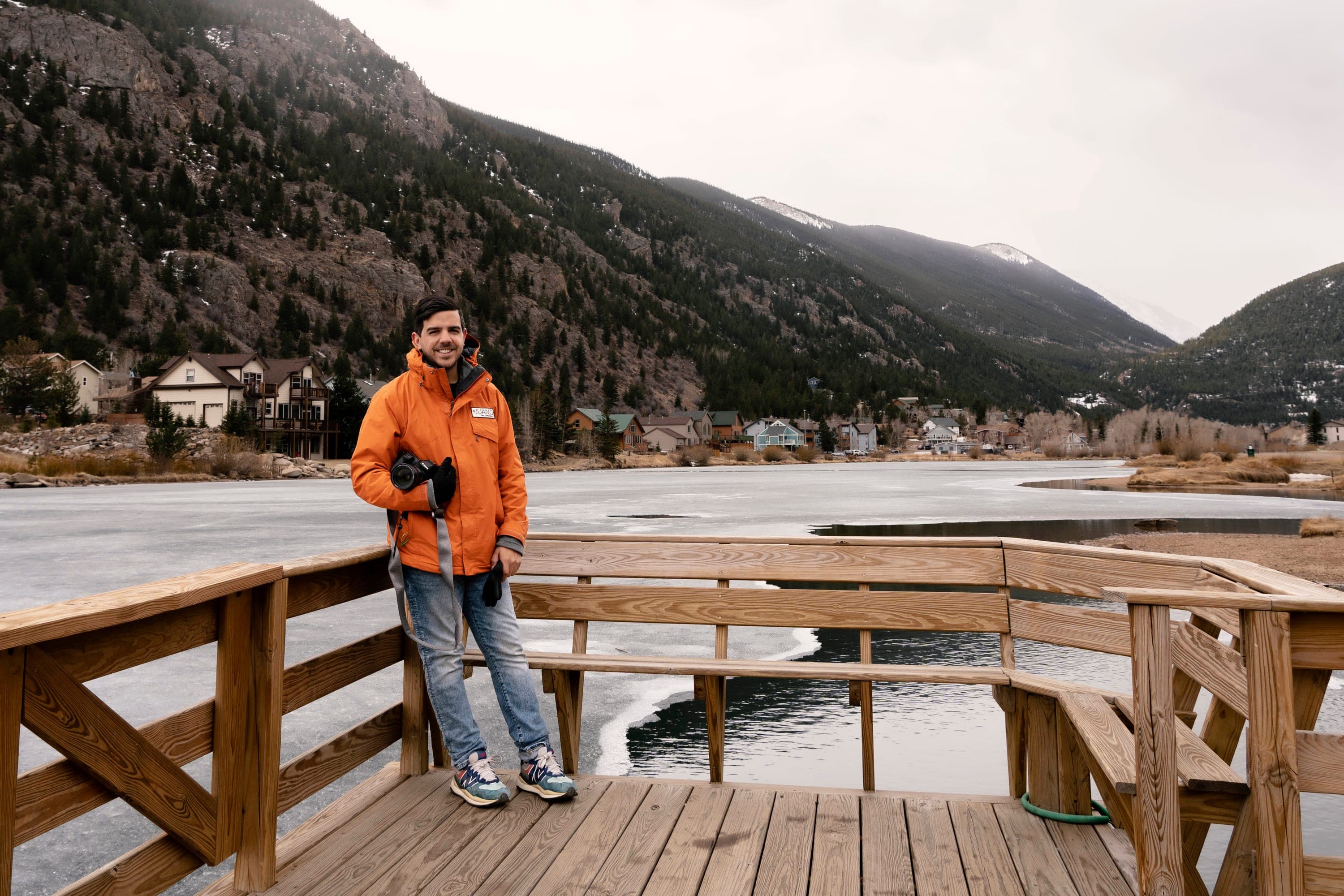 Juano with his camera on a wooden dock, in front of a frozen lake and the Colorado mountains